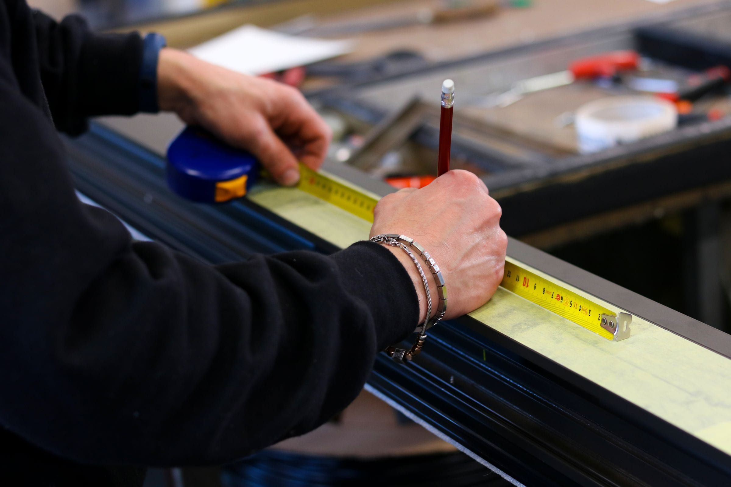 Vakman meet een aluminium profiel op met rolmaat en potlood